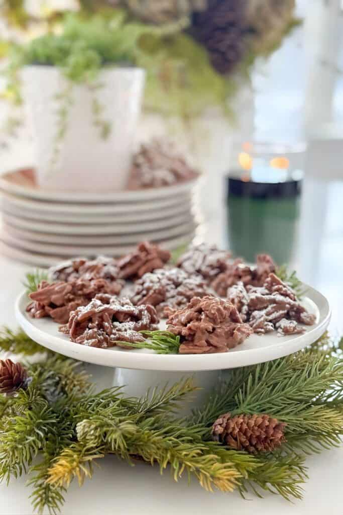 No bake haystack cookies on a white cake stand surrounded by Christmas greenery