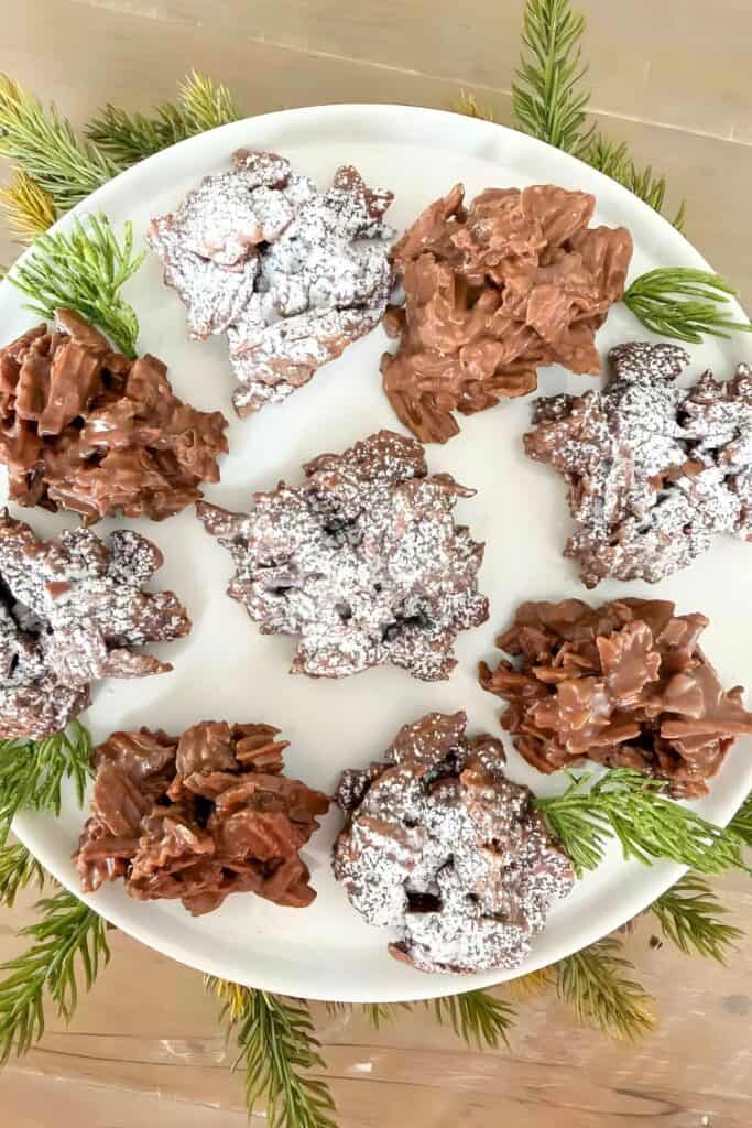 No bake haystack cookies arranged on a white plate with powdered sugar and Christmas greenery