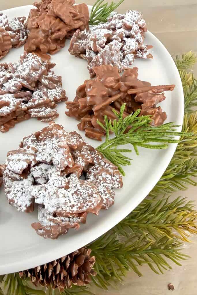 No bake haystack cookies dusted with powdered sugar on a white plate with Christmas greenery