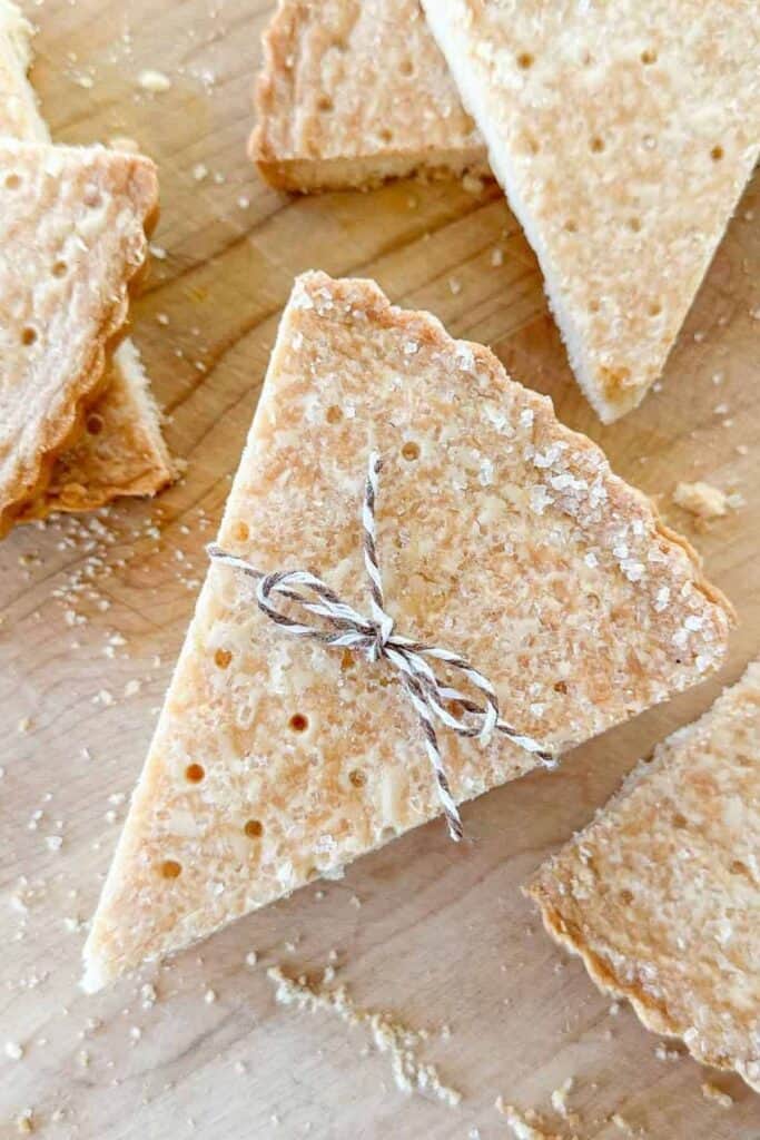 Buttery Scottish shortbread cookies cut into wedges and sprinkled with sugar on a wooden cutting board