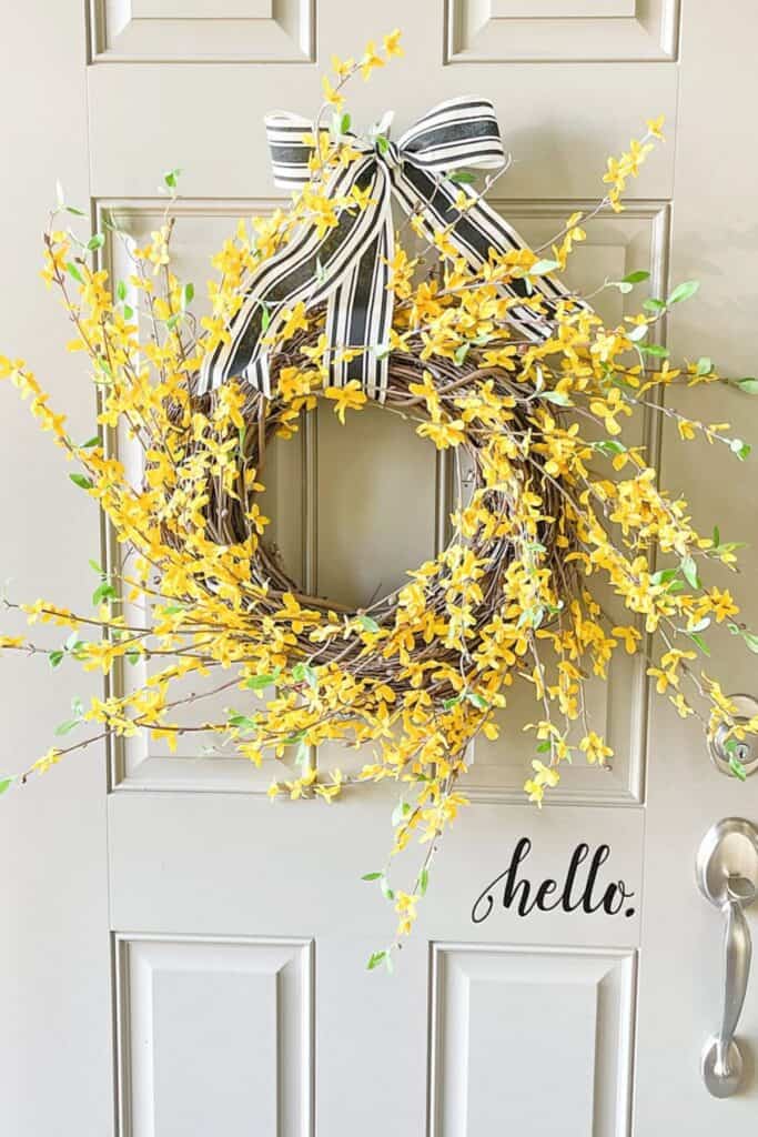 Brambly yellow forsythia wreath with a black and white bow hanging on a light colored front door.
