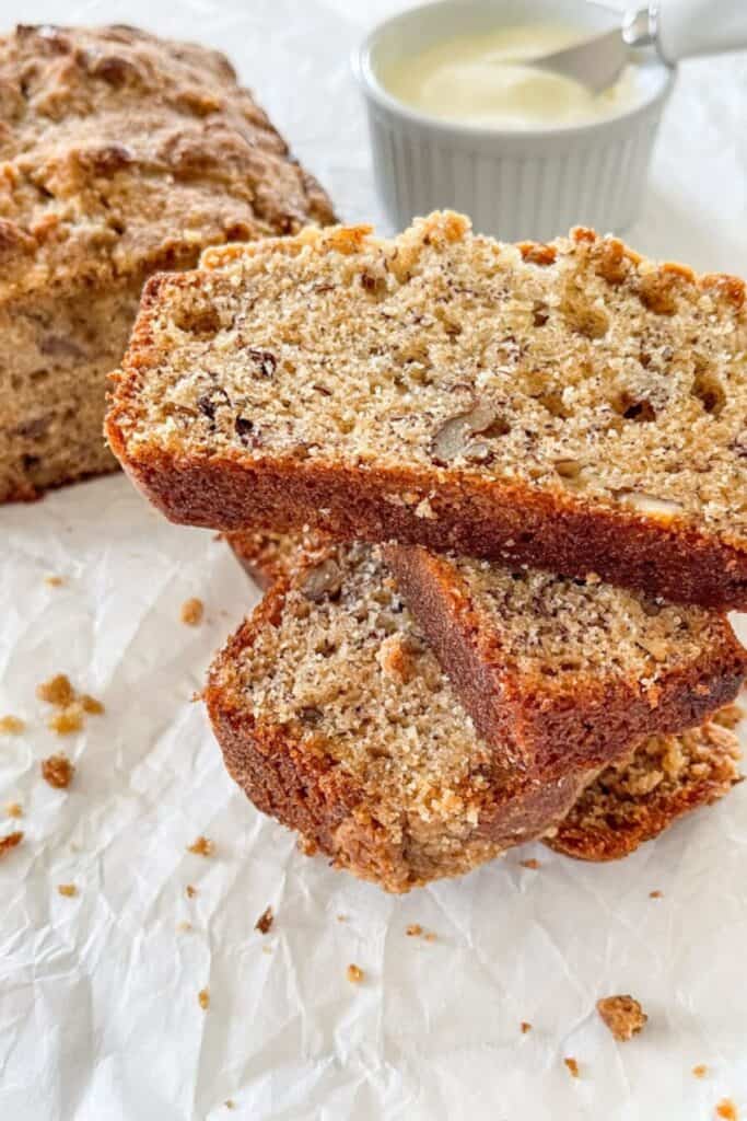 Streusel topped banana bread sliced on parchment paper with a small bowl of butter