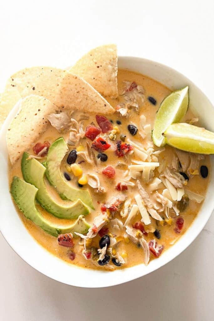 Creamy white chicken chili topped with avocado slices, tortilla chips, shredded cheese, and fresh lime wedges