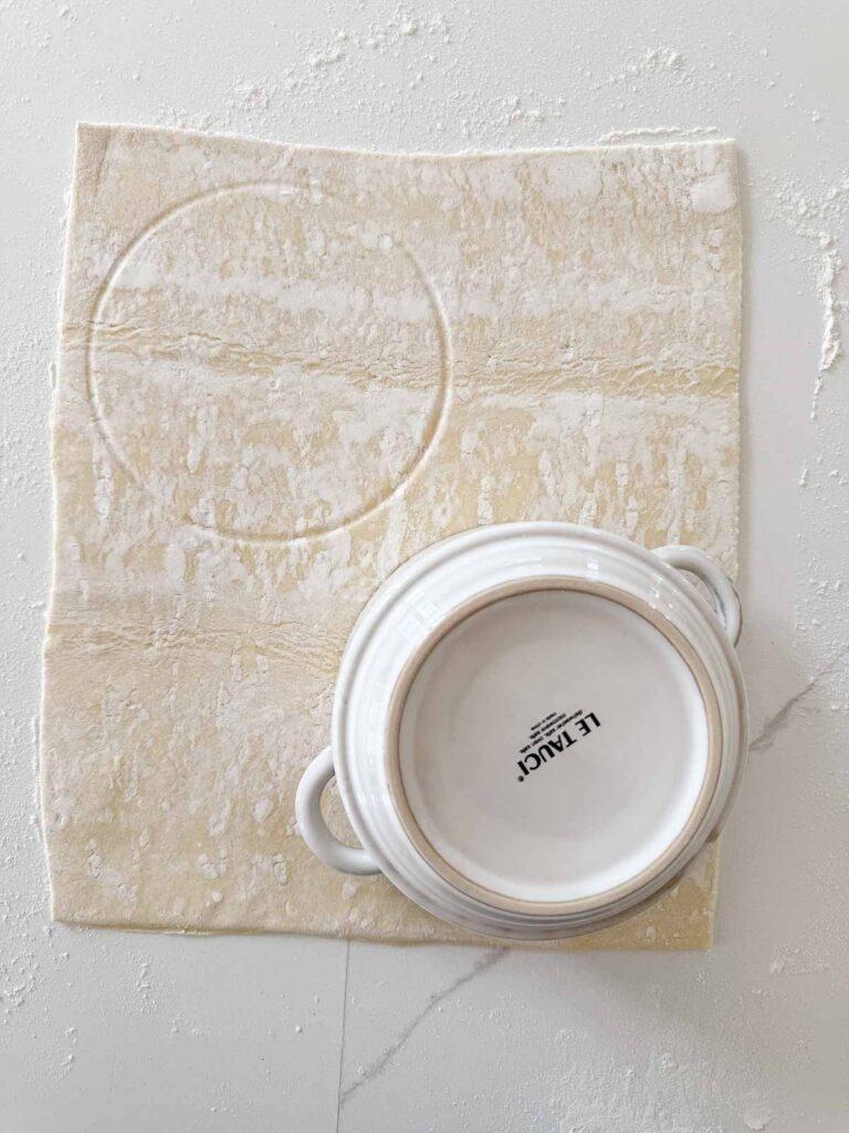 Puff pastry sheet with a bowl used to cut a round pastry lid for soup