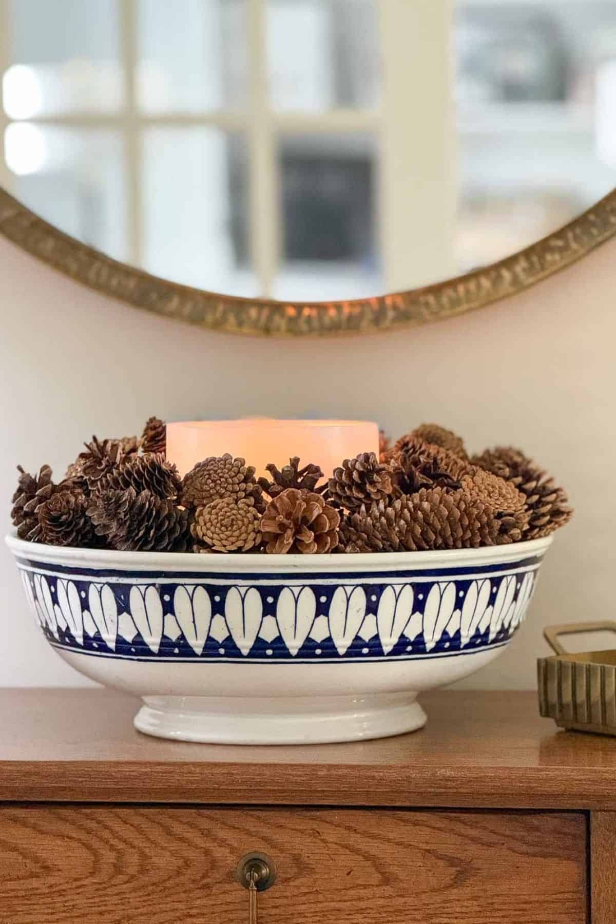 blue and white bowl filled with a candle and pinecones