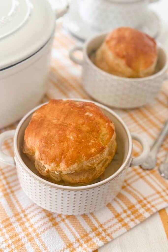 Individual bowls of sausage white bean and Swiss chard soup topped with baked puff pastry lids