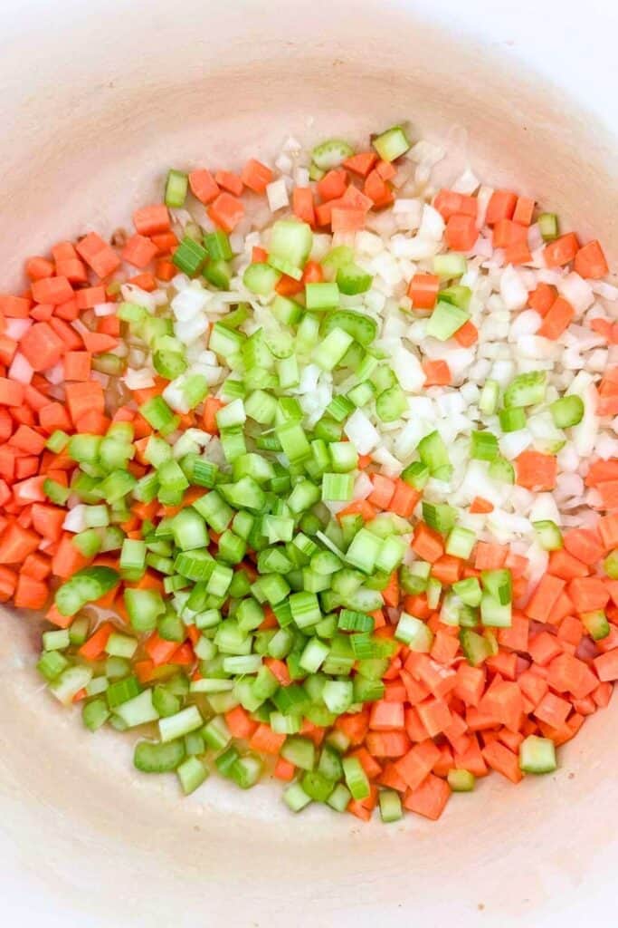Chopped onion, carrot, and celery sautéing in a pot for sausage white bean soup