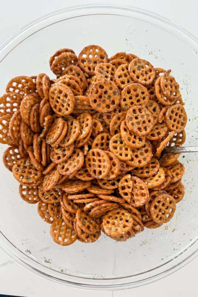 Seasoned ranch pretzel bites tossed with oil and seasoning in a glass bowl