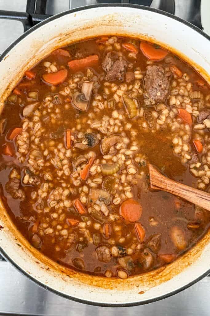 Beef barley soup simmering in a Dutch oven with carrots, mushrooms, pearl barley, and tender beef pieces in a rich broth.