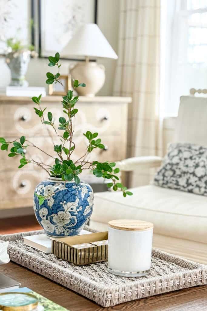 woven tray on coffee table styled with blue and white vase, greenery, candle, and decorative box for a collected look without clutter