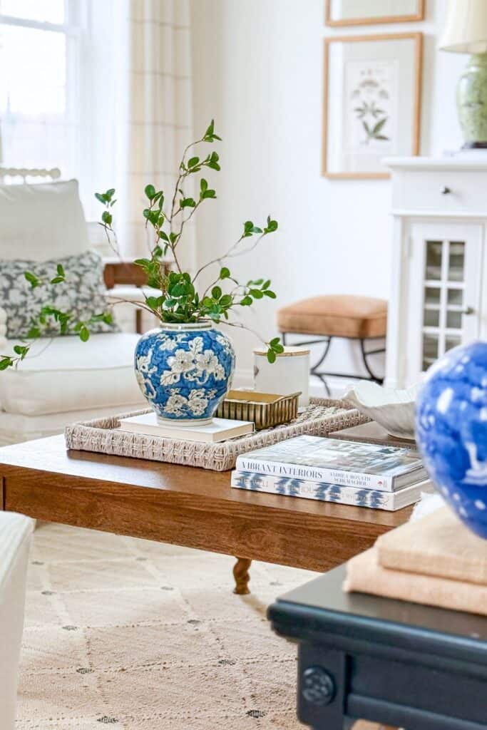 coffee table styled with blue and white vase, greenery, woven tray, stacked books, and balanced collected decor
