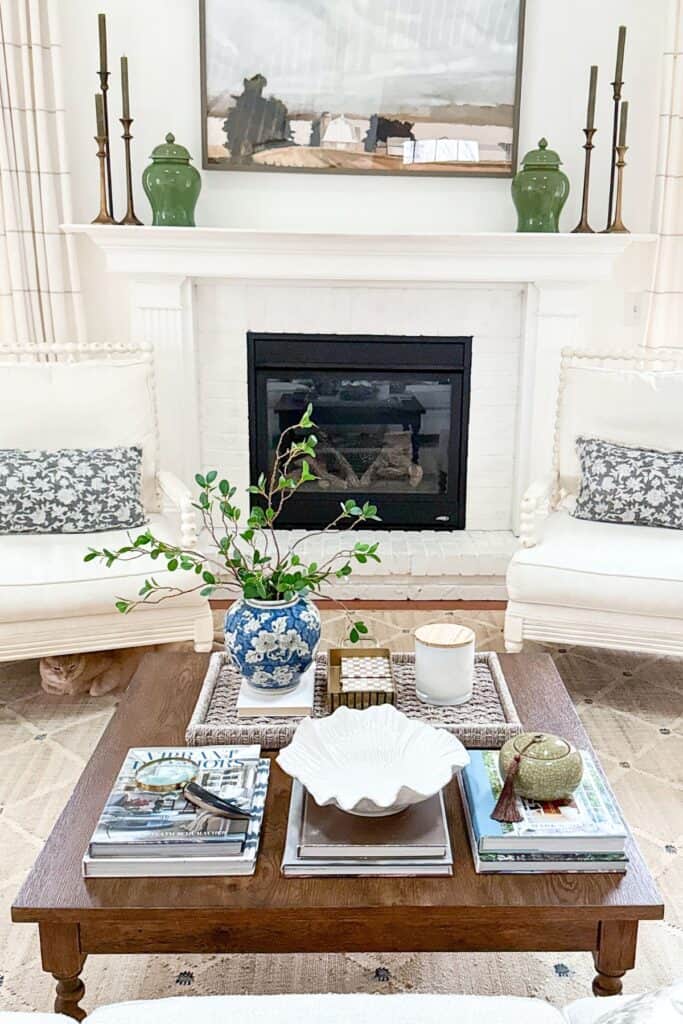 living room coffee table styled with stacked books, blue and white vase, tray, white bowl, and balanced decor in front of fireplace