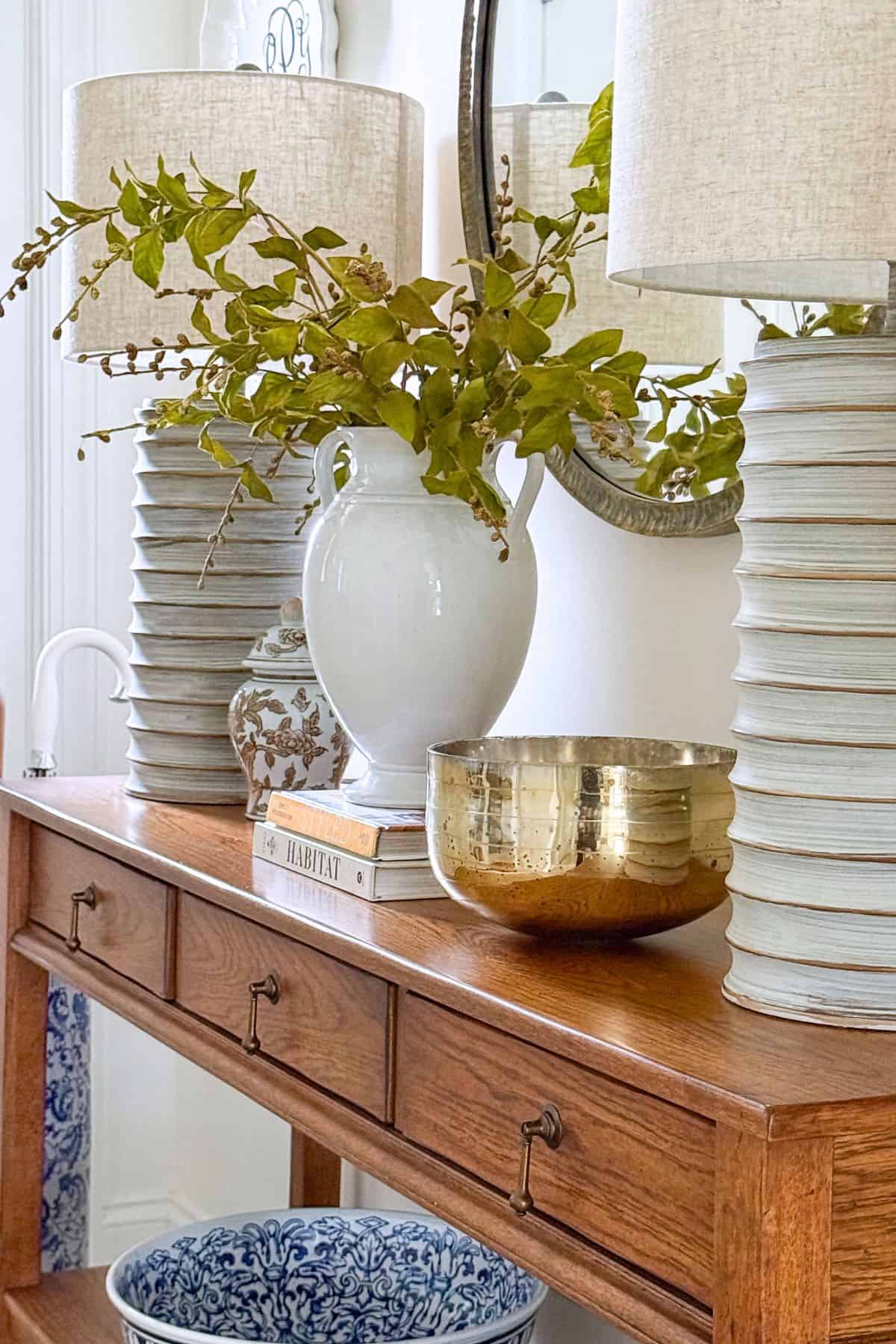 console table with two large lamps, an urn of greens and small accent decor.