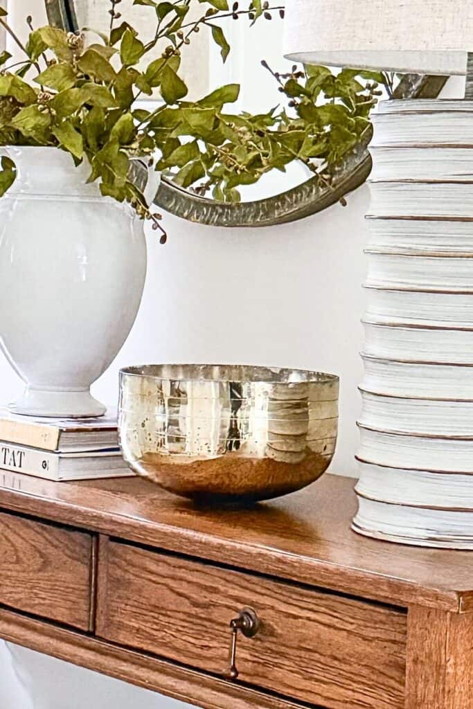 console table styled with white ceramic vase, greenery, textured lamp, and warm gold bowl for a collected look without clutter