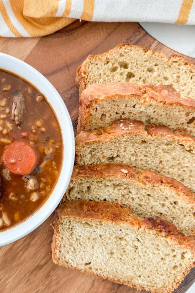 Close up of homemade beef barley soup served with sliced bread on a wooden board.
