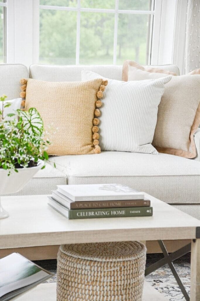 Neutral sofa with layered pillows and simple coffee table styling in a bright living room.