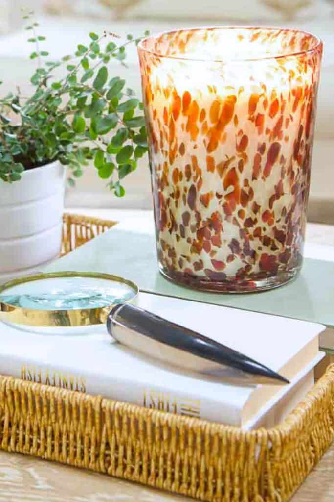 Lit candle in a patterned glass holder with a small potted plant and stacked books, creating a cozy February table vignette