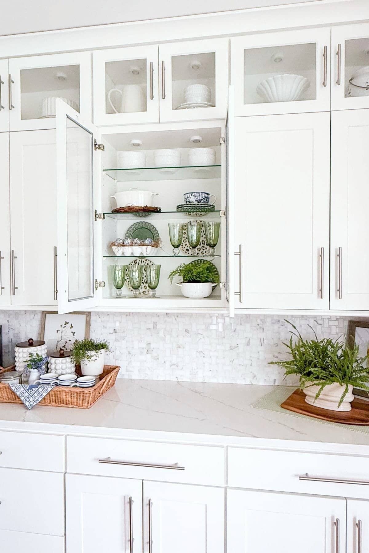 kitchen counter decorated for spring with glass front cabinets open, revealing spring dishes and decor