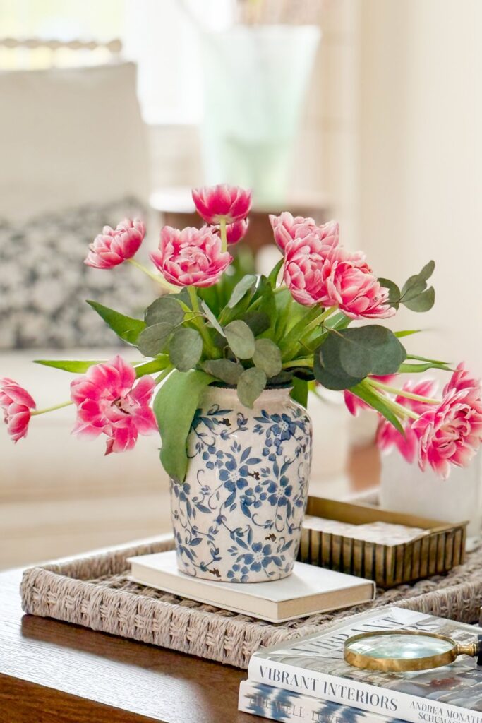 coffee table styled with pink flowers in blue and white vase on a tray with books and accents