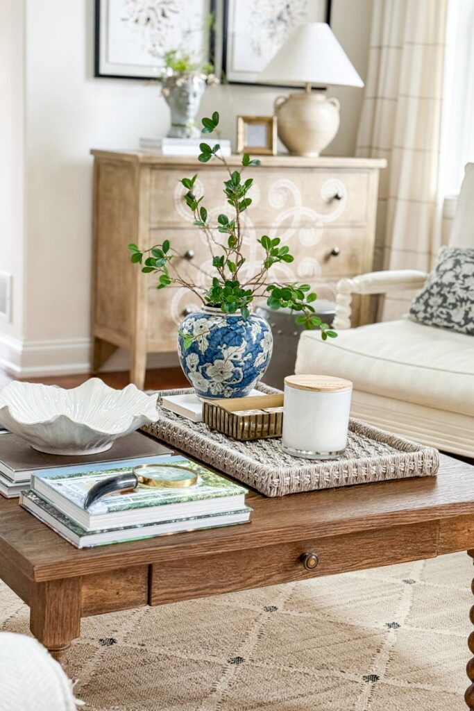 coffee table styled with woven tray, blue and white vase, books and candle in a neutral living room