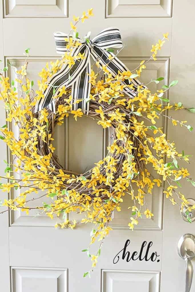Forsythia spring wreath with yellow blooms and striped ribbon hanging on a front door