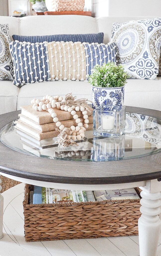 round coffee table styled with stacked books, wood beads, candle and small potted plant