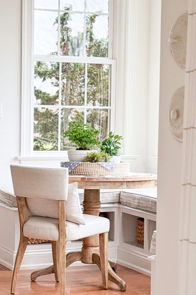 spring breakfast nook with round wooden table, banquette seating, and potted plants by a bright window