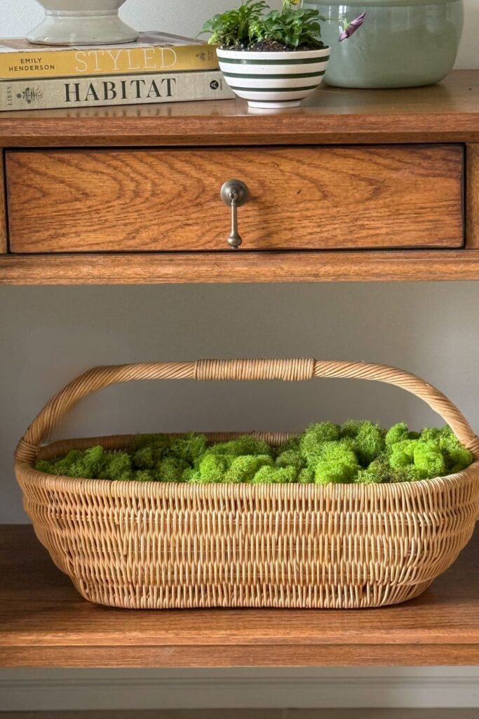 woven basket filled with green moss on lower shelf of wooden console table for spring decor