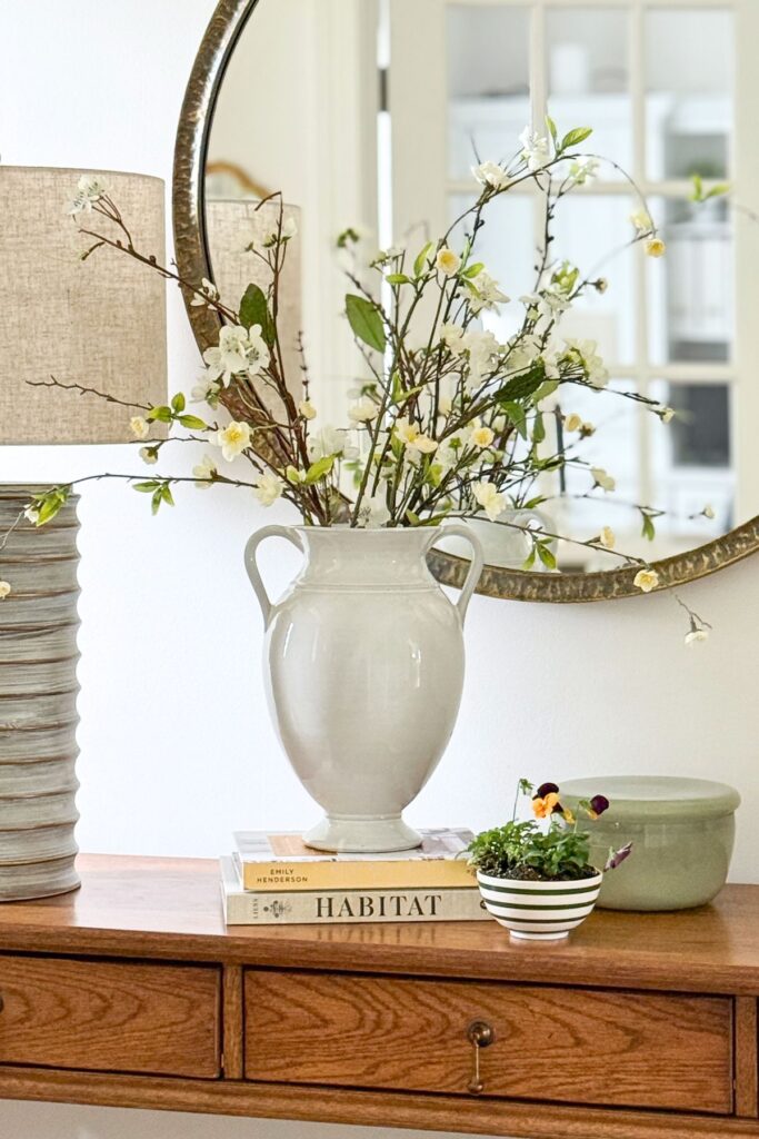 spring console table styled with white vase of flowering branches, books, and small potted flowers