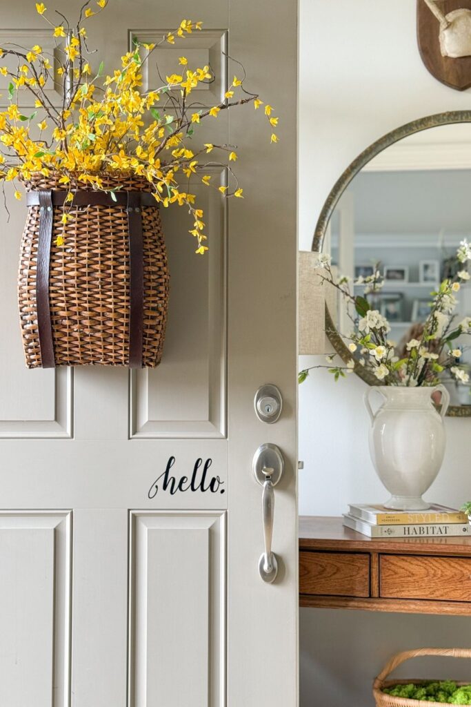 spring front door with woven basket filled with yellow flowering branches and view into foyer with white pitcher of branches