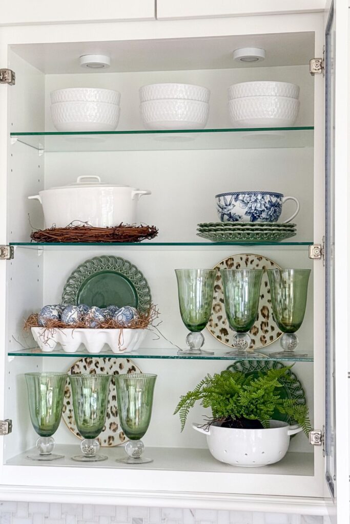 spring kitchen cabinet styled with green glassware, dishes, and simple seasonal decor