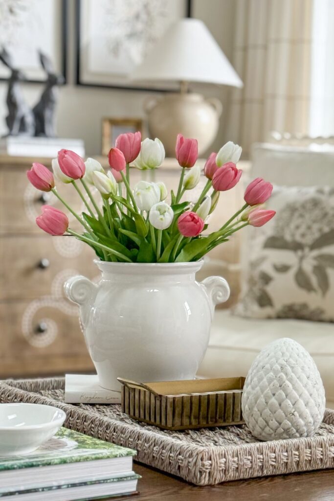 pink and white tulips arranged in a white vase on a woven tray with books and decorative accents on a coffee table