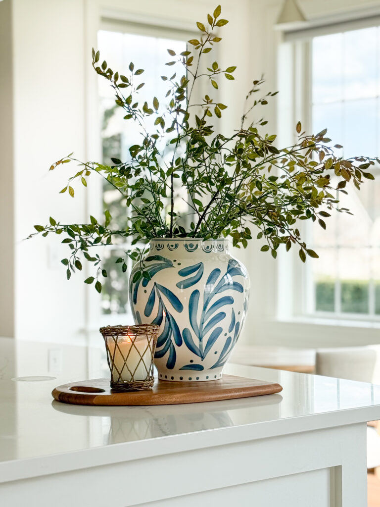 kitchen island styled with blue and white vase greenery and small candle on a wood board in a bright kitchen
