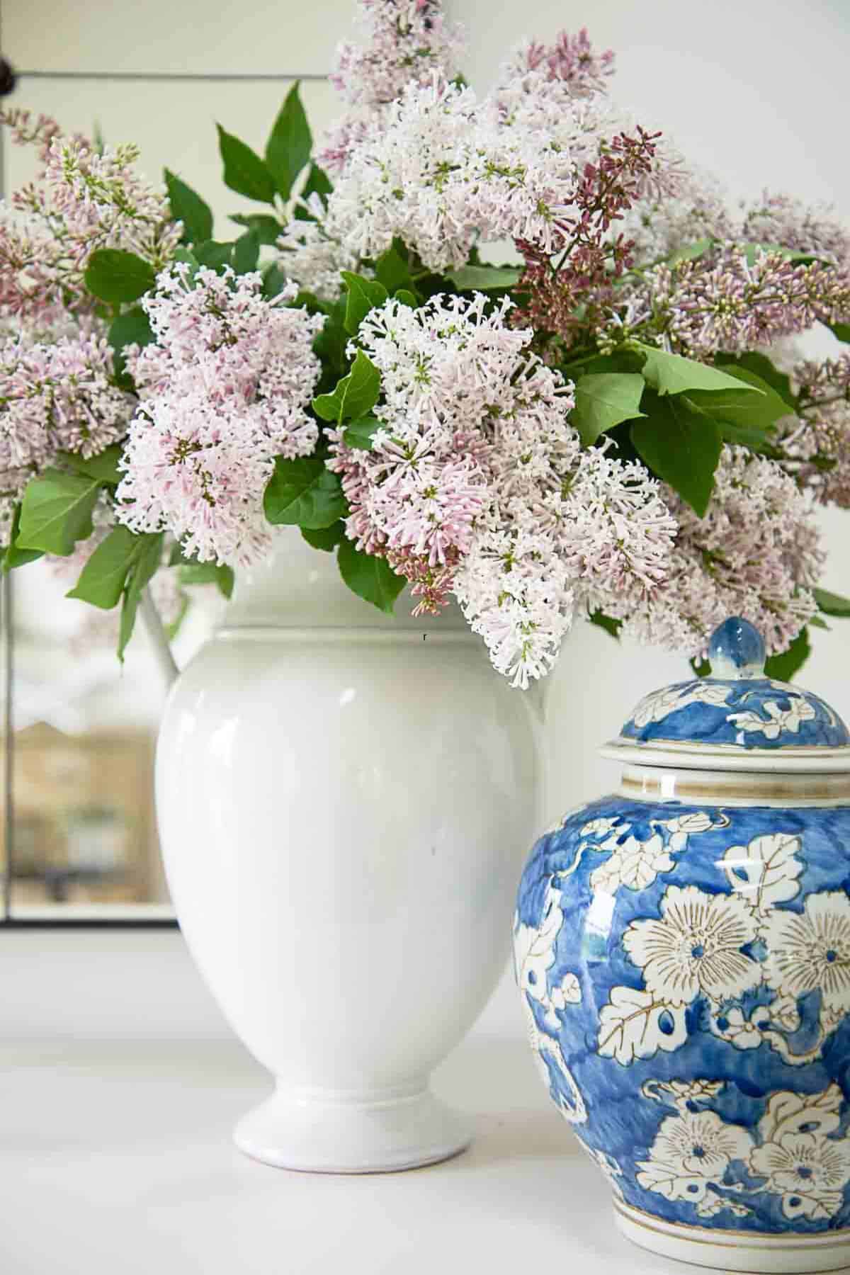 lilac branches in a white urn with a blue and white ginger jar sitting next to it.