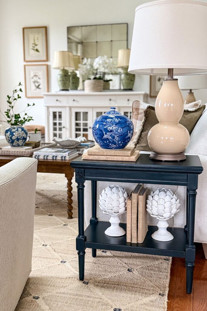 end table styled with lamp, stacked books, blue and white jar, and decorative accents in a neutral living room