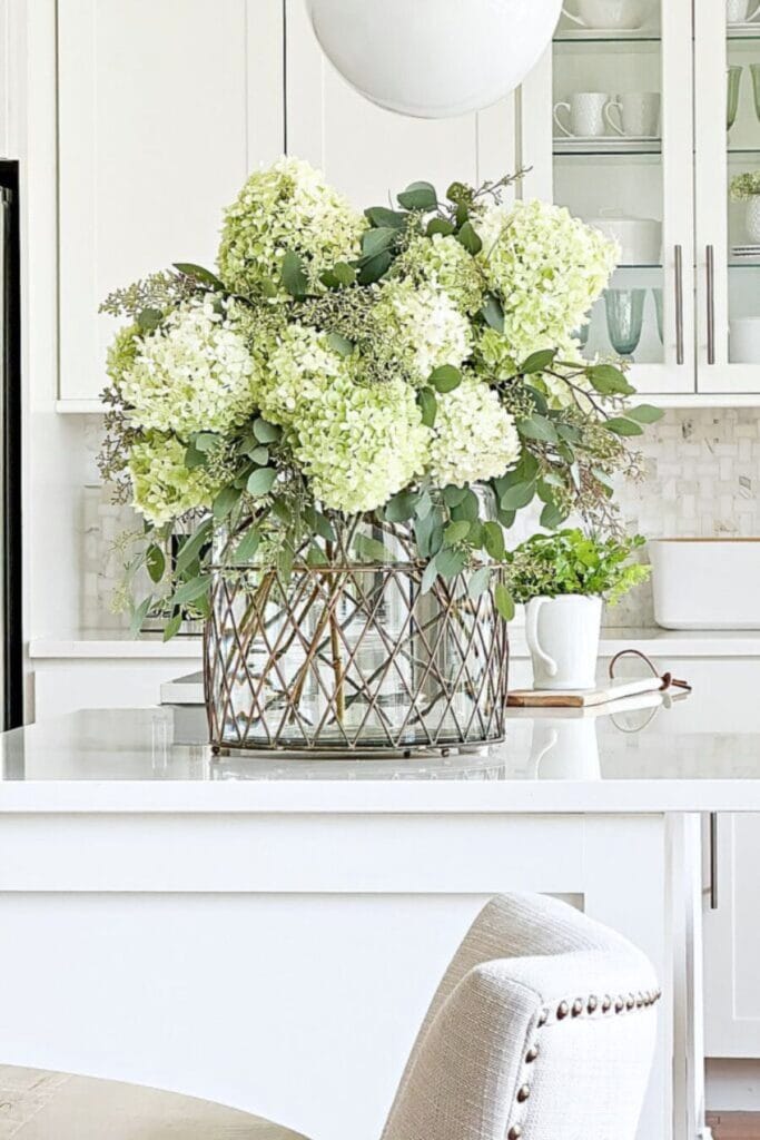 kitchen island styled with large hydrangea arrangement in a glass container as a centerpiece in a bright kitchen