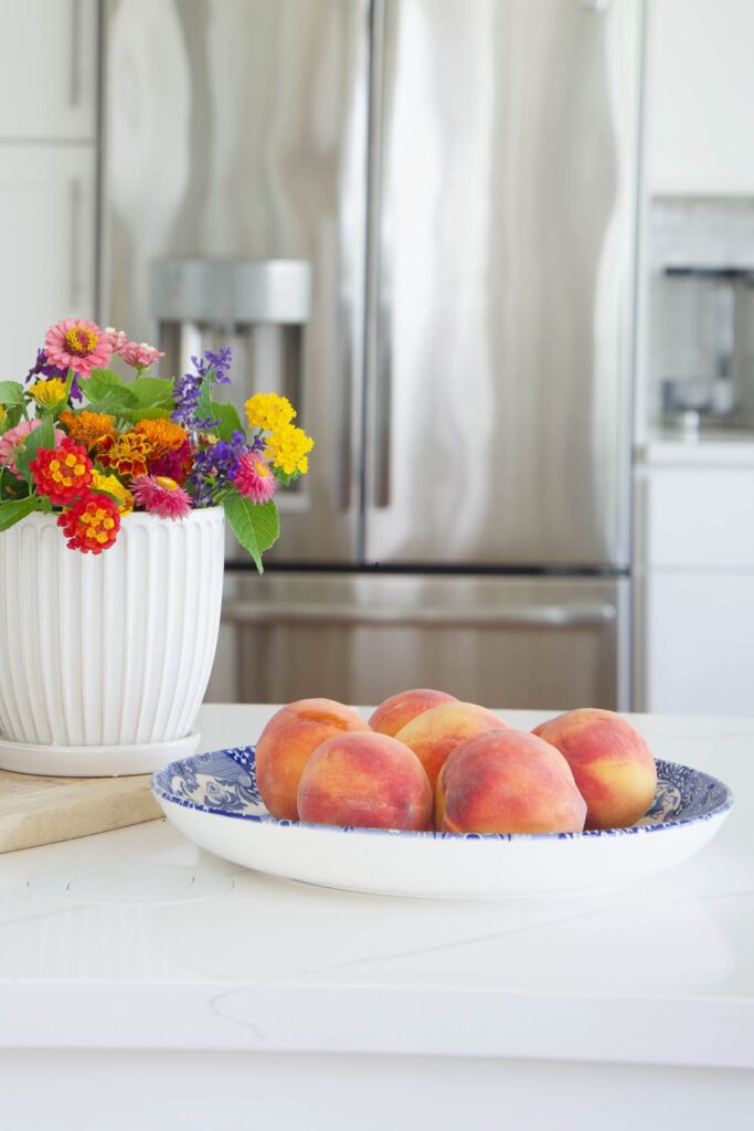 kitchen island styled with bowl of peaches and colorful flowers in a simple summer kitchen