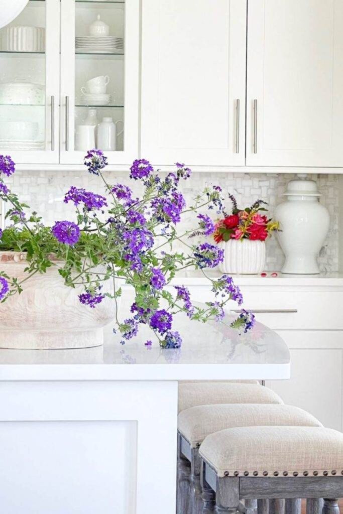 kitchen island styled with loose purple flowers in a large vase as a simple centerpiece in a white kitchen