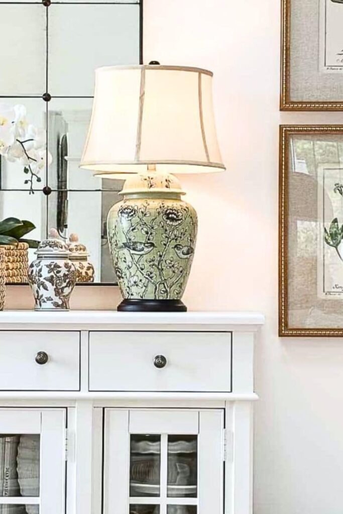 green chinoiserie lamp on a white buffet with mirror and framed art in a neutral living room