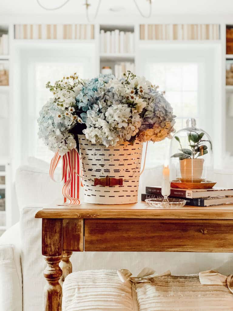 Vintage table with white bucket of blue hydrangeas and red and white striped ribbon