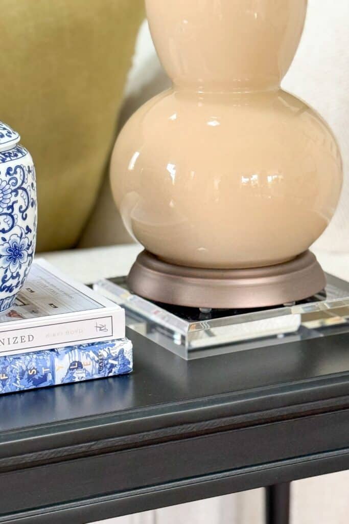 Table lamp styled on an acrylic riser on a small black end table with books and blue and white decor
