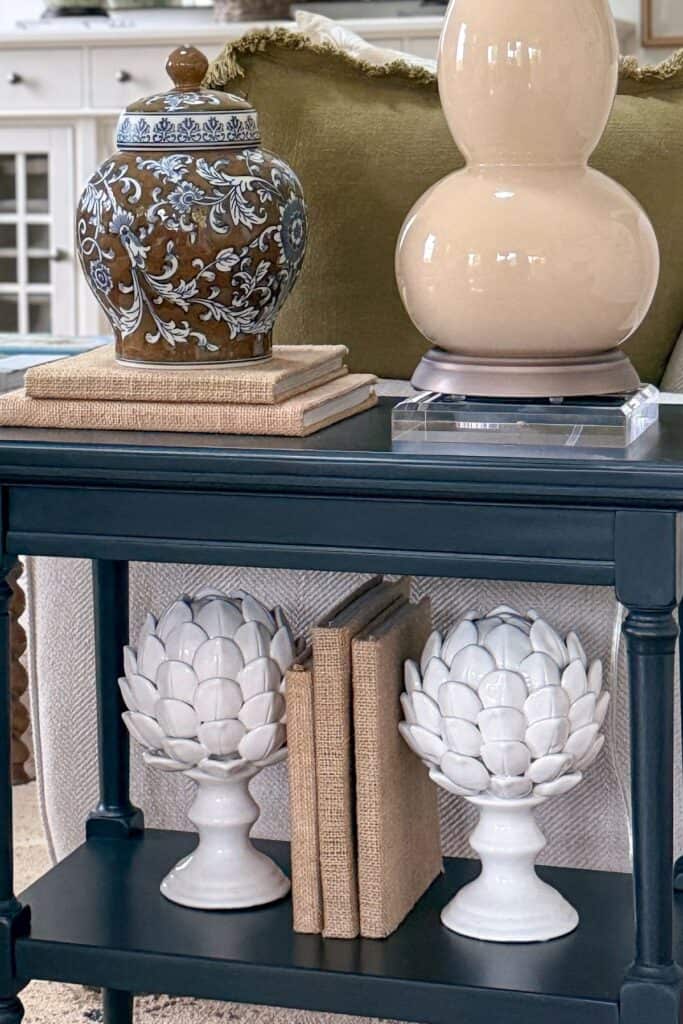 Small black end table with balanced shelf styling using books and white ceramic accessories in a neutral living room