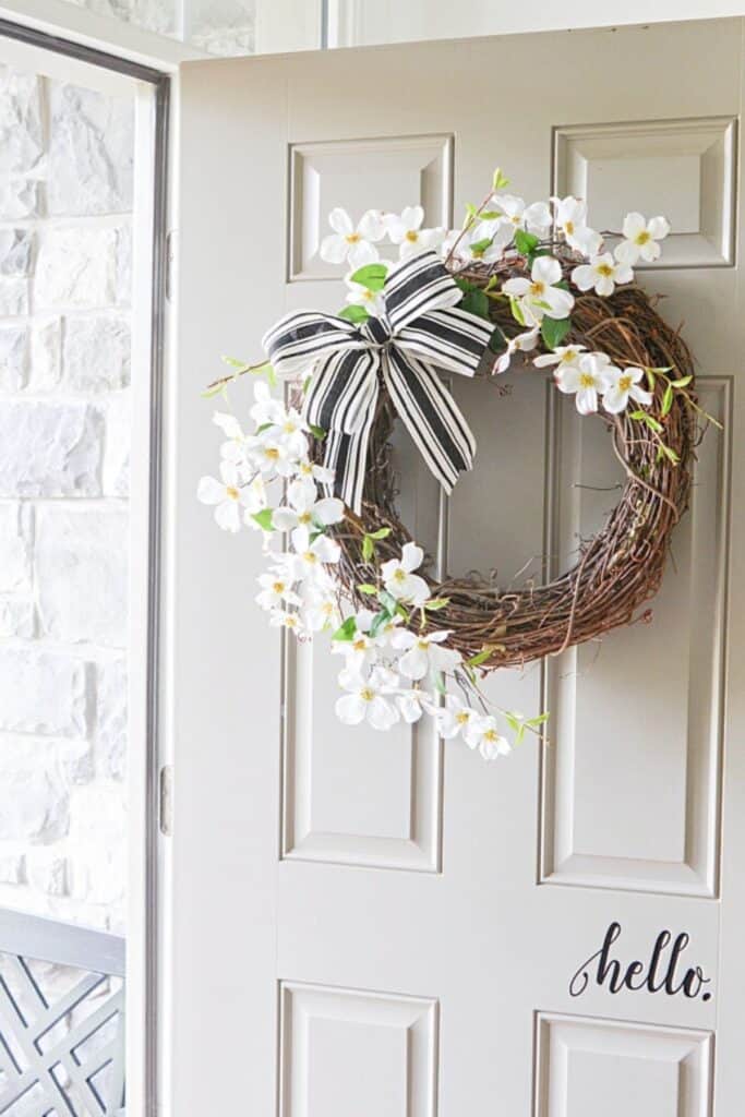 Dogwood summer wreath with black and white ribbon on an open front door with welcome decal
