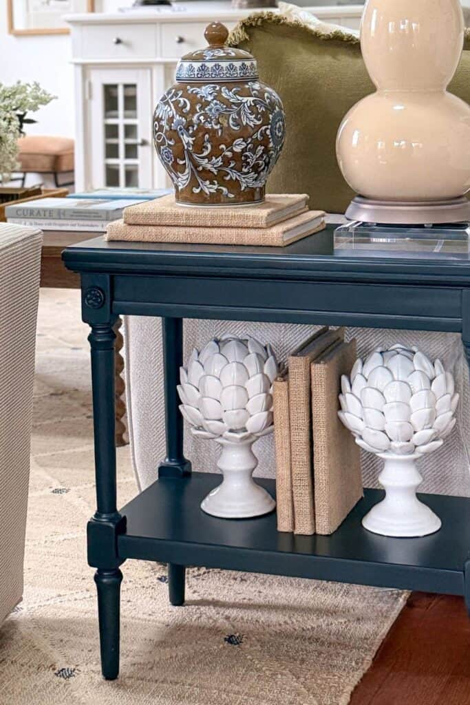 Small black end table with shelf decor styled using books, white ceramic accessories, stacked books, lamp, and decorative ginger jar