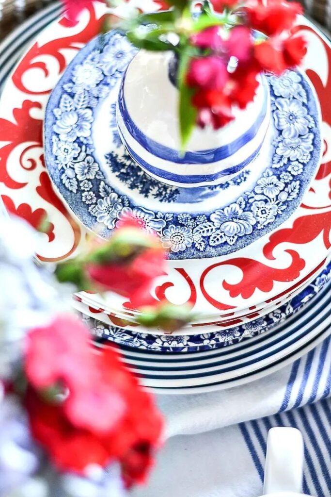 stacked red and blue transferware plates with a blue and white striped napkin and fresh red flowers for patriotic summer decorating