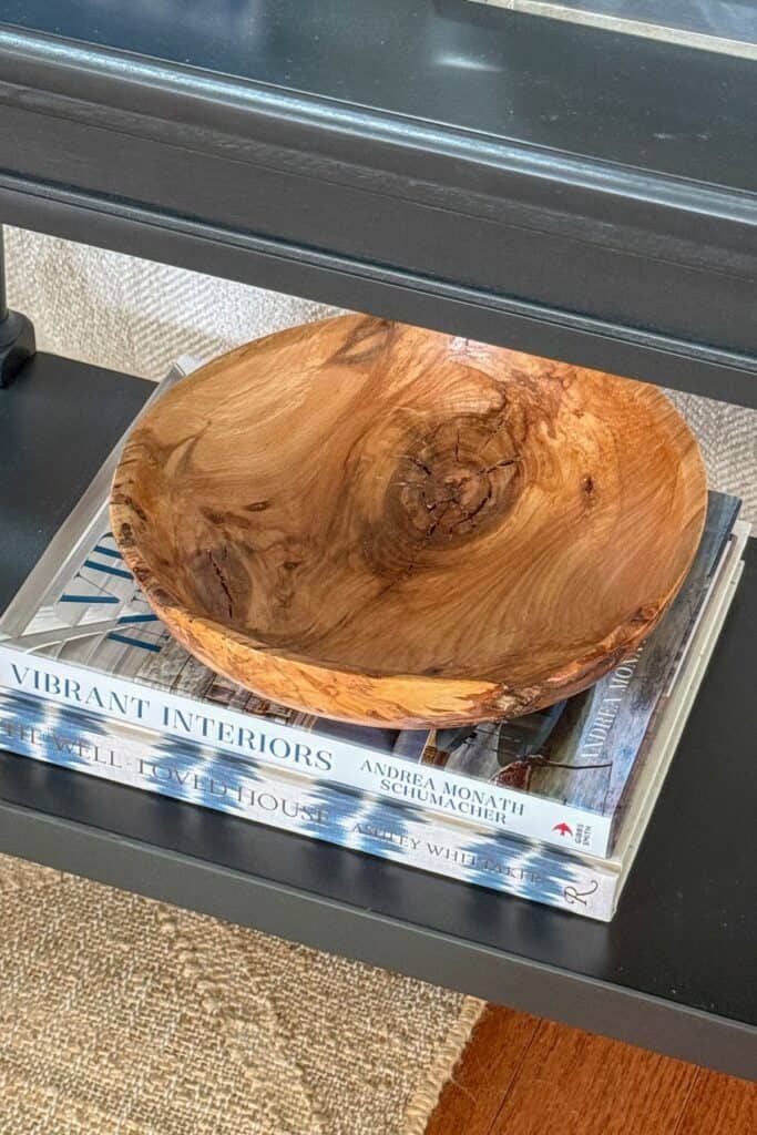End table shelf decorated with stacked coffee table books and a wooden bowl on a black side table