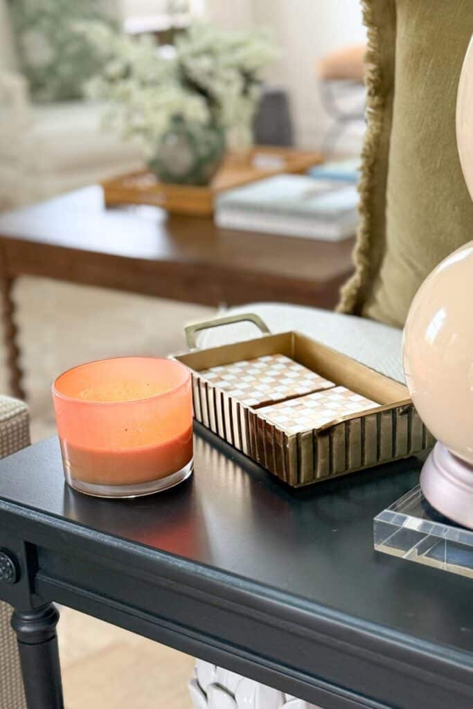Small black end table styled with a candle, decorative tray, and lamp in a cozy neutral living room