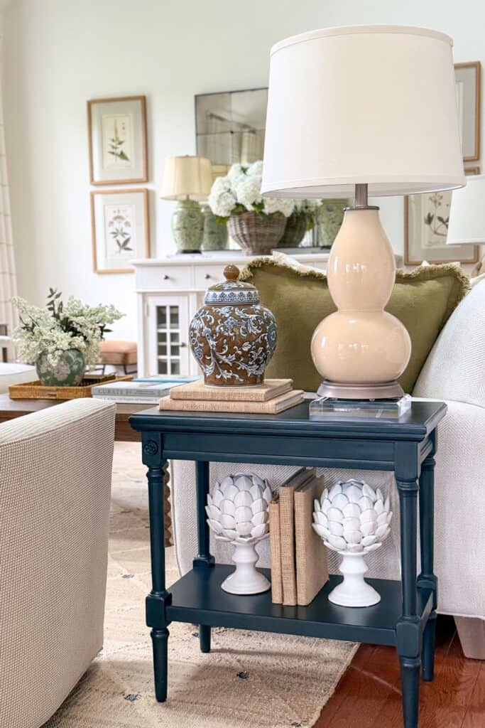 Small black end table styled with a lamp, decorative ginger jar, books, and shelf decor in a neutral living room