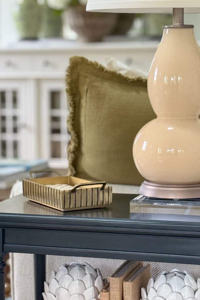 Small black end table styled with a lamp, decorative tray, books, and shelf decor in a neutral living room