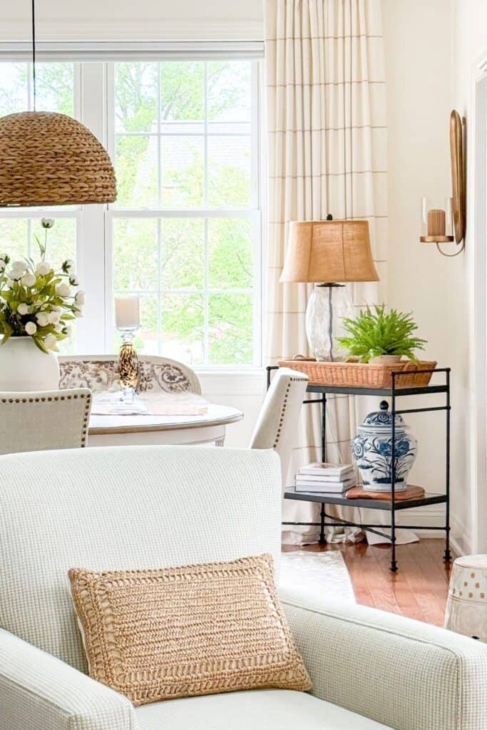 ight filled summer living room with a woven pendant light, blue and white ginger jar, fern, natural texture pillow, and white floral arrangement near large windows